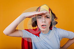 Brunette serious girl in yellow crown looking in distance. Close-up portrait of curly young lady in red mantle isolated