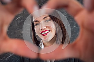 Brunette with short hair and red lipstick shows heart sign