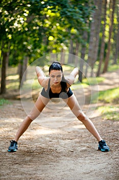 Brunette slim young woman in sportswear workout outside, doing stretching exercises of body in park