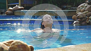 Brunette smiles woman enjoys water in swimming pool in slow motion on sunny day while vacation with beautiful sun