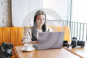 Brunette smiling young woman photographer working with her camera and laptop in the cafe