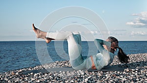 Brunette sportswoman training abdominal muscle lying on pebble beach sunset coastline