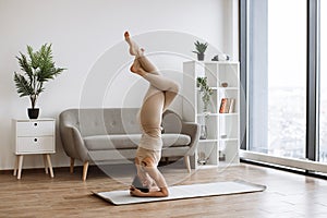 Brunette staying in headstand pose at bright commodious living room.