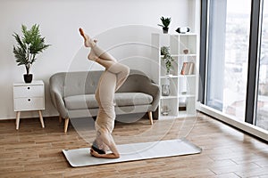 Brunette staying in headstand pose at bright commodious living room.