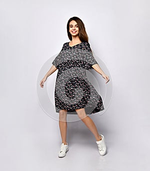 Brunette teenage girl in black dress with floral print and white sneakers. She smiling, posing isolated on white. Full length