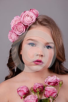 Brunette teenage girl with pink roses in her hair on gray background. flowers in curls on the head. fashion photo