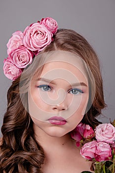 Brunette teenage girl with pink roses in her hair on gray background. flowers in curls on the head. fashion photo