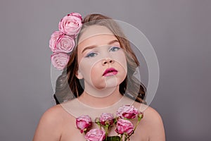Brunette teenage girl with pink roses in her hair on gray background. flowers in curls on the head. fashion photo