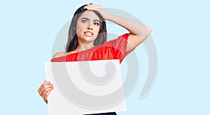 Brunette teenager girl holding blank empty banner stressed and frustrated with hand on head, surprised and angry face