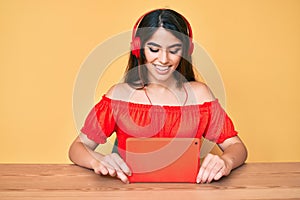 Brunette teenager girl using touchpad wearing headphones smiling with a happy and cool smile on face