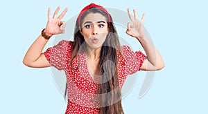 Brunette teenager girl wearing summer dress looking surprised and shocked doing ok approval symbol with fingers
