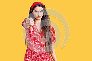 Brunette teenager girl wearing summer dress looking unhappy and angry showing rejection and negative with thumbs down gesture