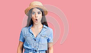 Brunette teenager girl wearing summer hat afraid and shocked with surprise expression, fear and excited face