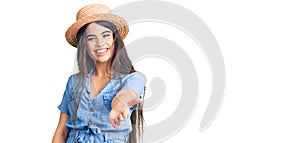 Brunette teenager girl wearing summer hat smiling friendly offering handshake as greeting and welcoming