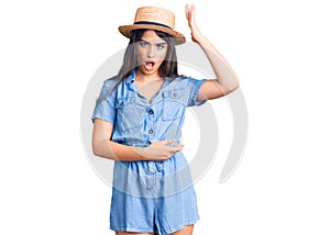 Brunette teenager girl wearing summer hat surprised with hand on head for mistake, remember error