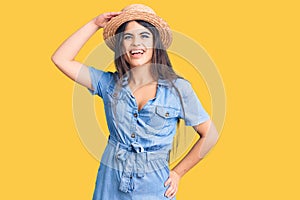 Brunette teenager girl wearing summer hat very happy and smiling looking far away with hand over head