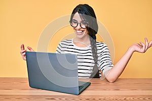 Brunette teenager girl working using computer laptop celebrating victory with happy smile and winner expression with raised hands