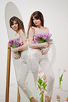 brunette topless at the mirror in a room with bouquets of tulips on the floor