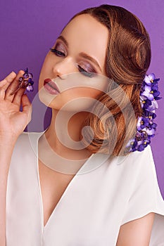 Brunette on a violet background. Girl with professional make-up and hairstyle. Beauty salon. Girl with blue flowers in her hair. W