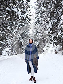 Brunette walks through the winter forest in a gray hat, blue sweater and blue coat.