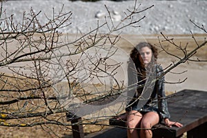 Brunette wavy hair girl in the mountains, sitting sexy on a massive wooden table.