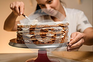 Brunette in white clothes spreading thick, greasy cream on cakes