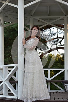 Brunette in a white dress in the park next to a white wooden pergola photo