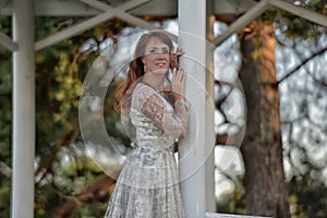 Brunette in a white dress in the park next to a white wooden pergola photo