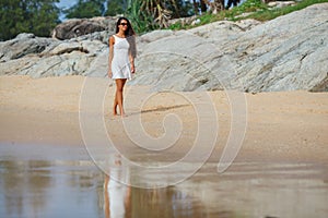 Brunette in white dress walking along the beach