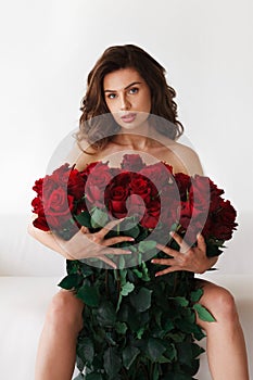 Brunette on a white sofa with a large bouquet of red roses