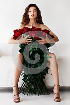 Brunette on a white sofa with a large bouquet of red roses