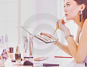 Brunette woman applying make up for a evening date in front of a mirror