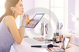 Brunette woman applying make up for a evening date in front of a mirror