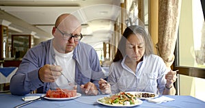 Brunette woman and bald man are lunching in cafe in daytime, enjoying meal