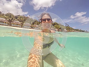 Brunette woman in bikini and sunglasses swimming taking a selfie