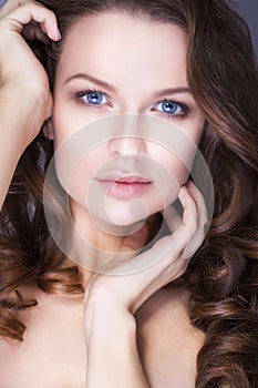 Brunette woman with blue eyes without make up, natural flawless skin and hands near her face