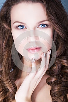Brunette woman with blue eyes without make up, natural flawless skin and hands near her face