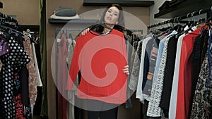 Brunette woman choosing sweater from rack with hangers inside room