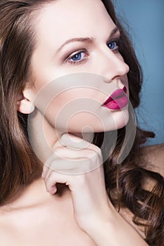 Brunette woman with creative make up violet eye shadows full red lips, blue eyes and curly hair with her hand on her face