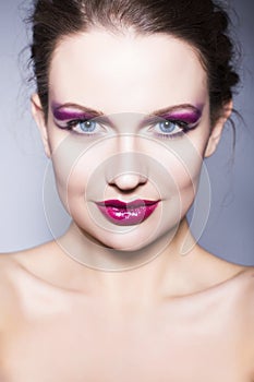 Brunette woman with creative make up violet eye shadows full red lips, blue eyes and curly hair with her hand on her face