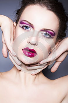 Brunette woman with creative make up violet eye shadows full red lips, blue eyes and curly hair with her hand on her face