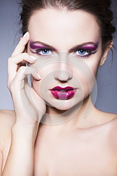 Brunette woman with creative make up violet eye shadows full red lips, blue eyes and curly hair with her hand on her face