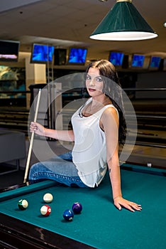 Brunette woman with cue near billiard table