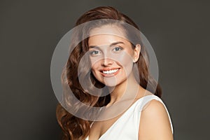 Brunette woman with curly beautiful hair smiling on gray background