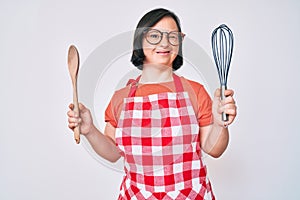 Brunette woman with down syndrome cooking using baker whisk and spoon winking looking at the camera with sexy expression, cheerful