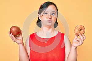 Brunette woman with down syndrome holding red apple and donut sitting looking at the camera blowing a kiss being lovely and sexy