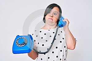 Brunette woman with down syndrome holding vintage telephone clueless and confused expression