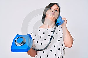 Brunette woman with down syndrome holding vintage telephone looking at the camera blowing a kiss being lovely and sexy