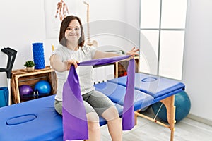 Brunette woman with down syndrome traning arms resistance with elastic bands at physiotherapy clinic