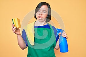 Brunette woman with down syndrome wearing apron holding scourer clueless and confused expression